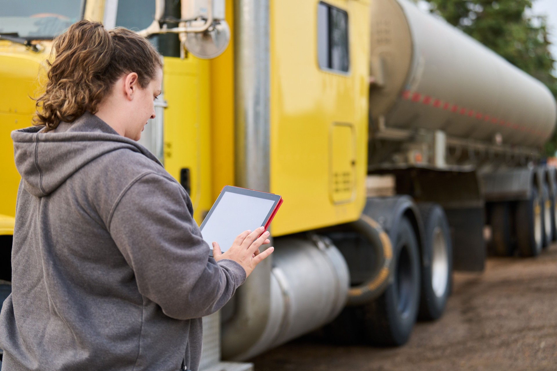 Female trucker driver standing by her tanker truck and checking a tablet